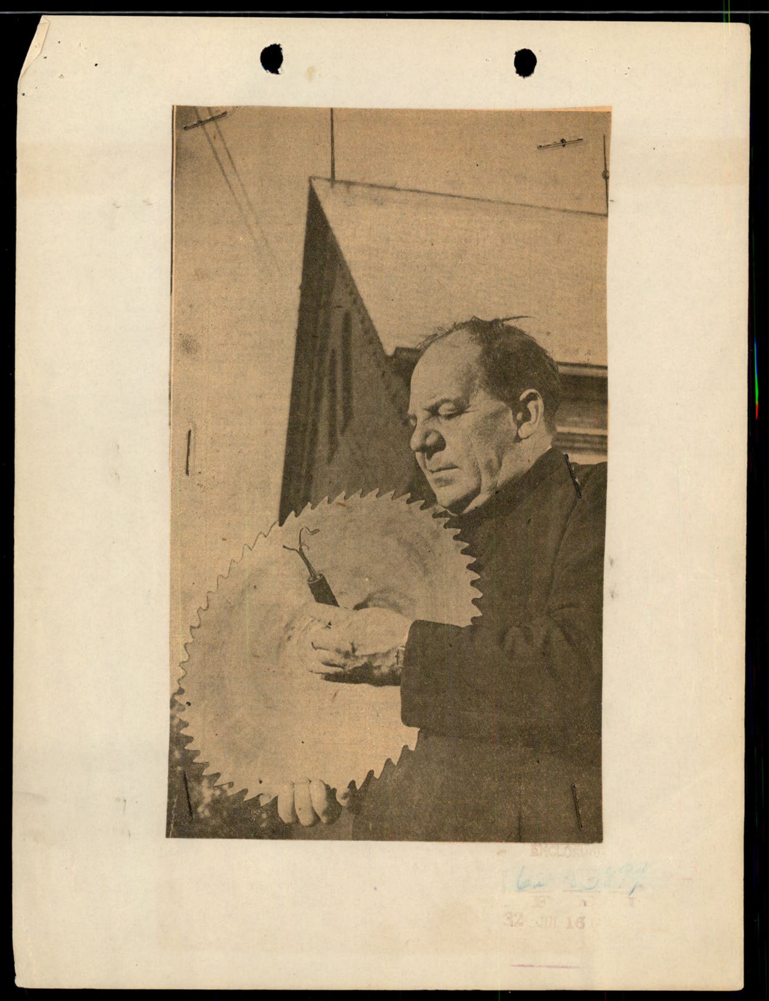 A man, identified in other clippings as Father Joseph Brasky, holds a large circular saw blade.