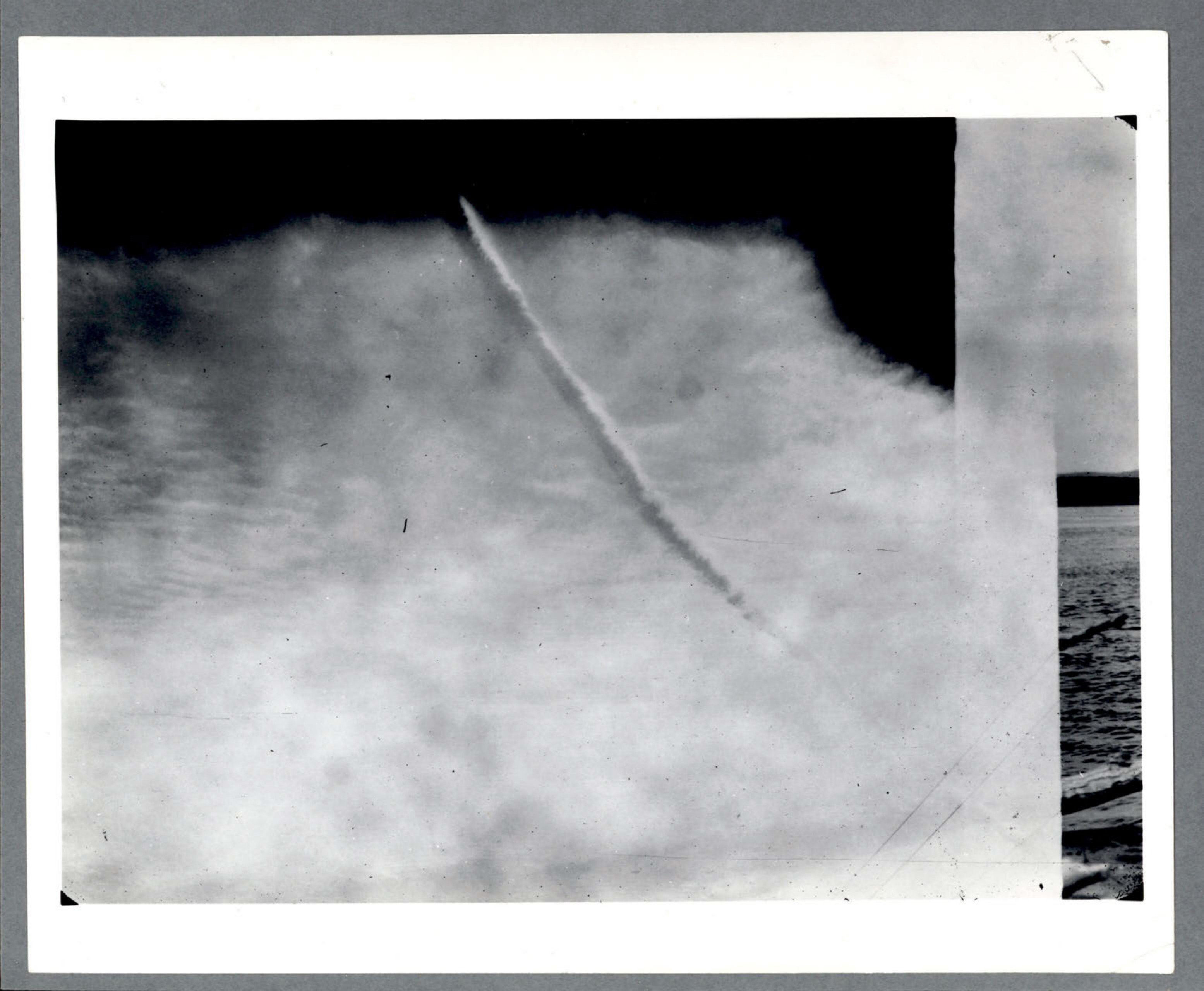 Photograph of a contrail or object trail in a cloudy sky.
