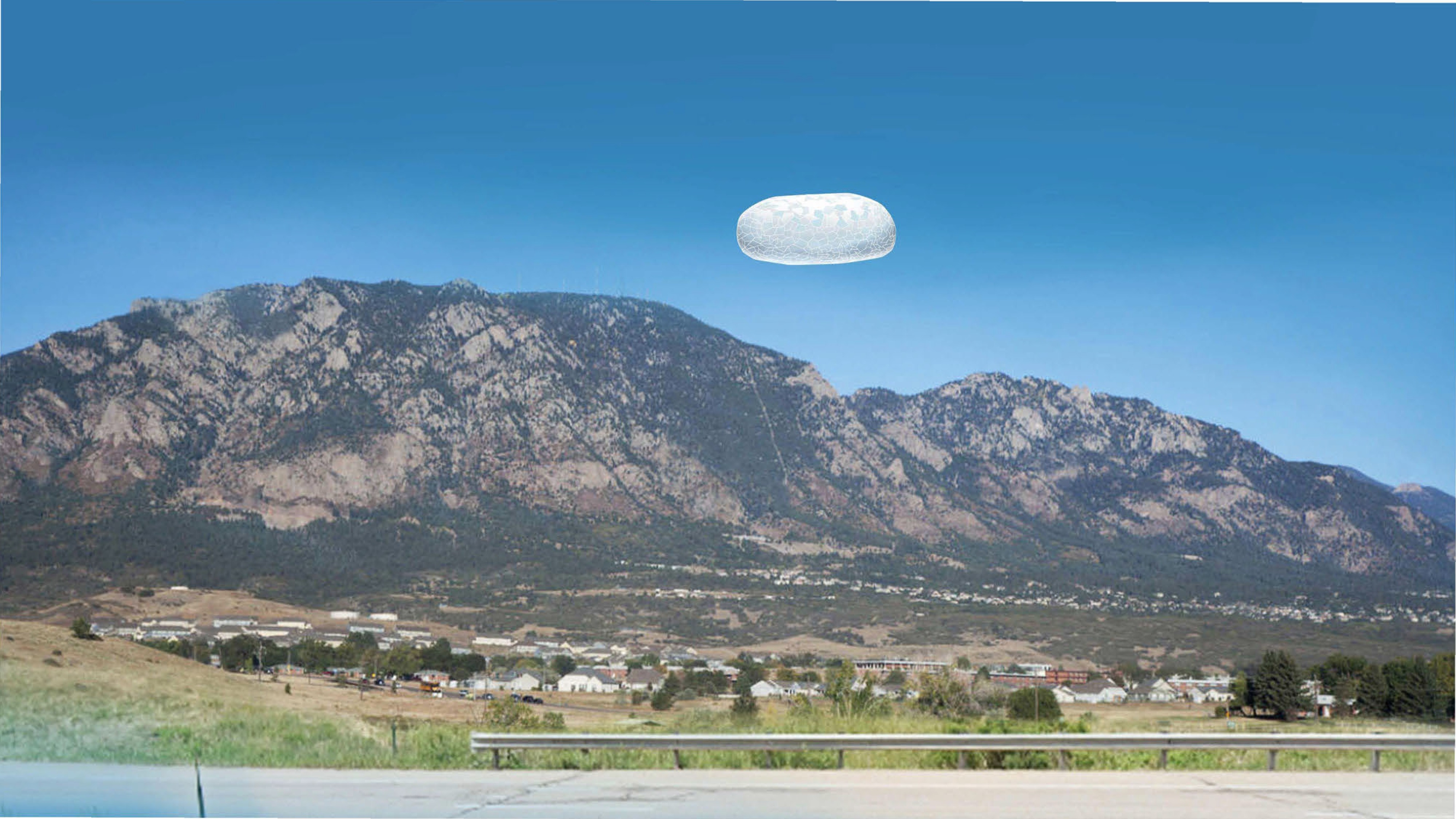 A photograph of a pill-shaped, translucent object hovering in the sky above a mountain range and a small town.